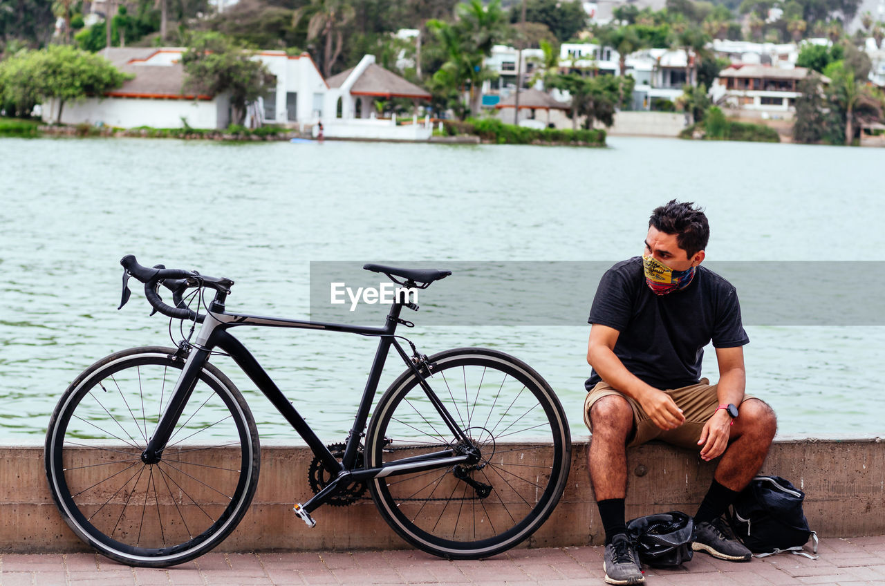 Young man sitting on bicycle by water