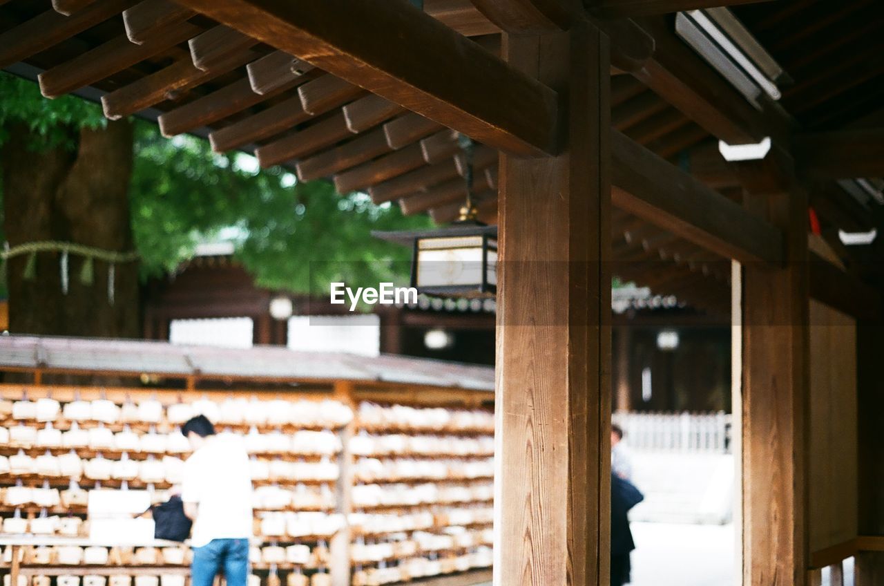 Rear view of man standing by prayer blocks at meiji-jingu shrine