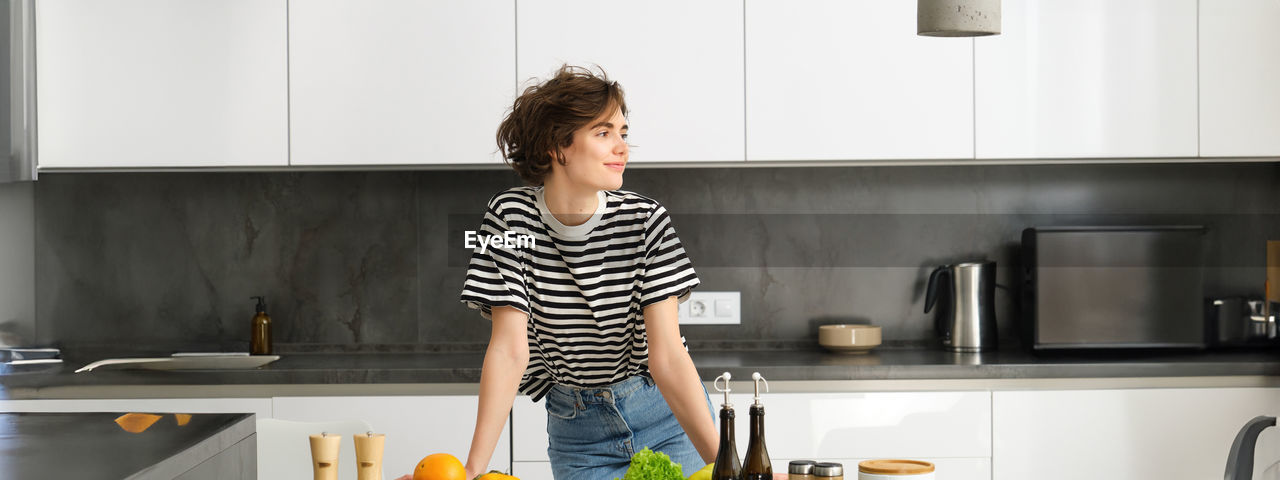 portrait of young woman standing in kitchen at home