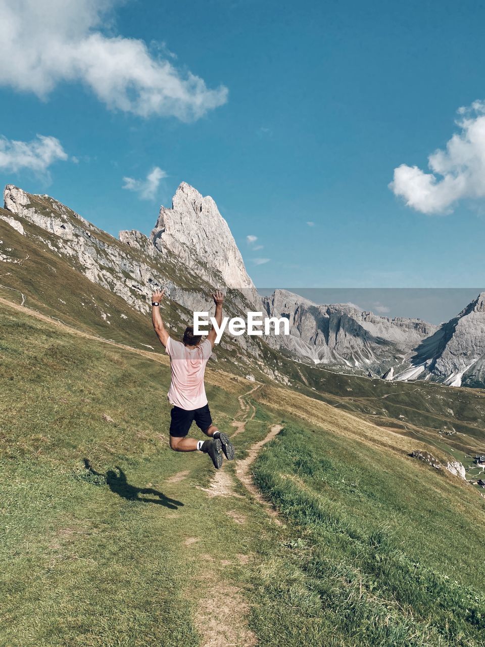 Rear view of man jumping in front of mountain range against sky