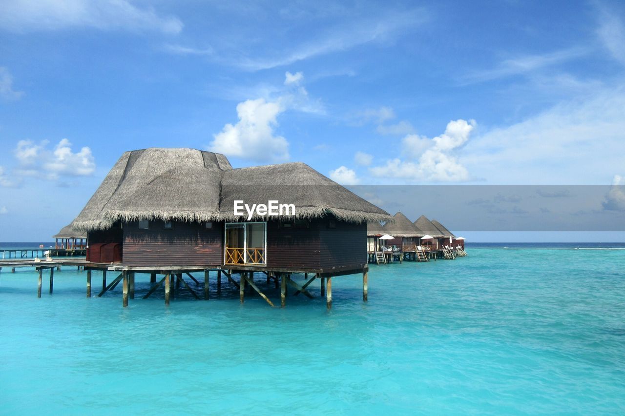 Stilt house over sea against blue sky