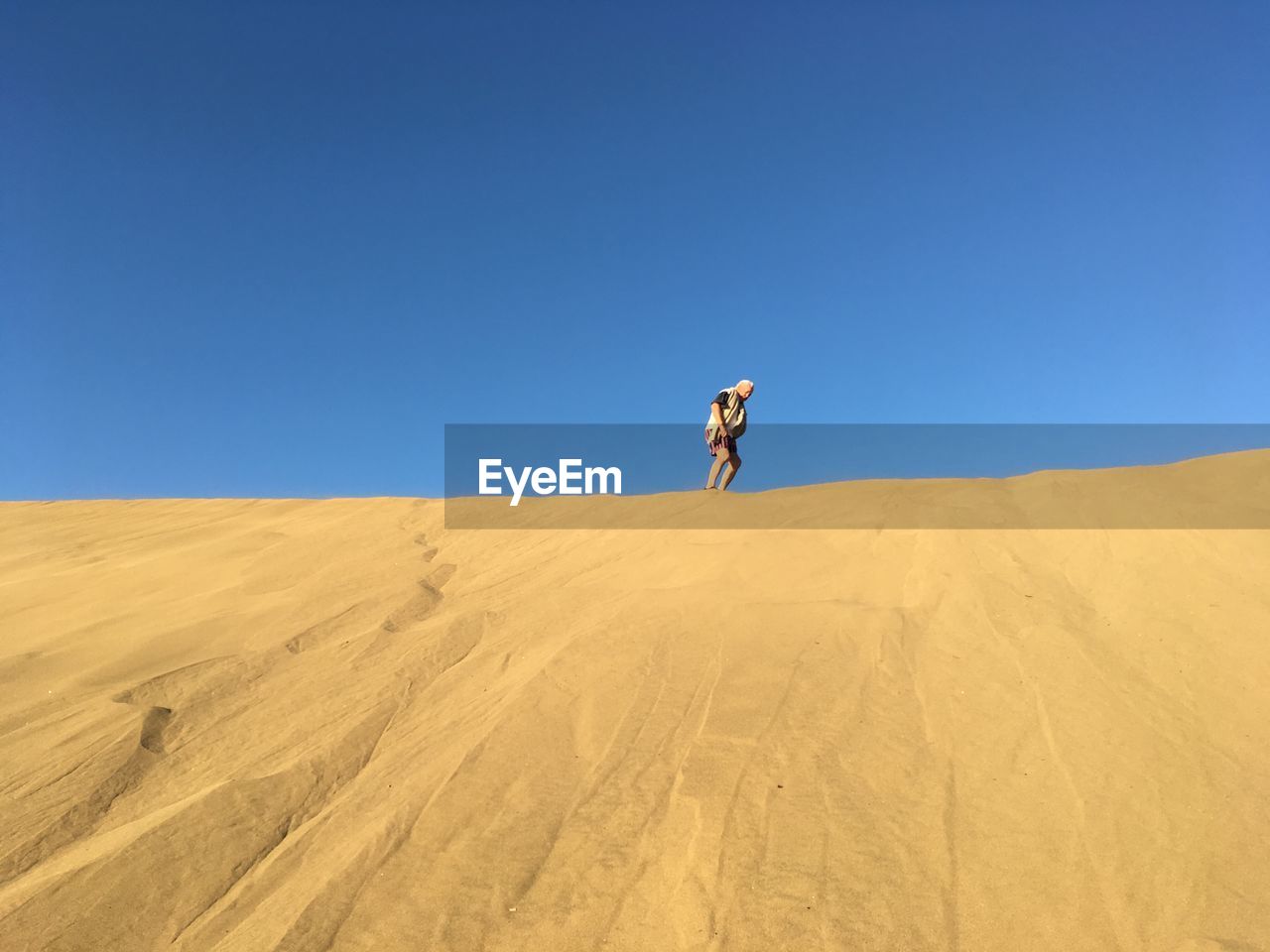 Low angle view of mature man standing at desert against clear blue sky