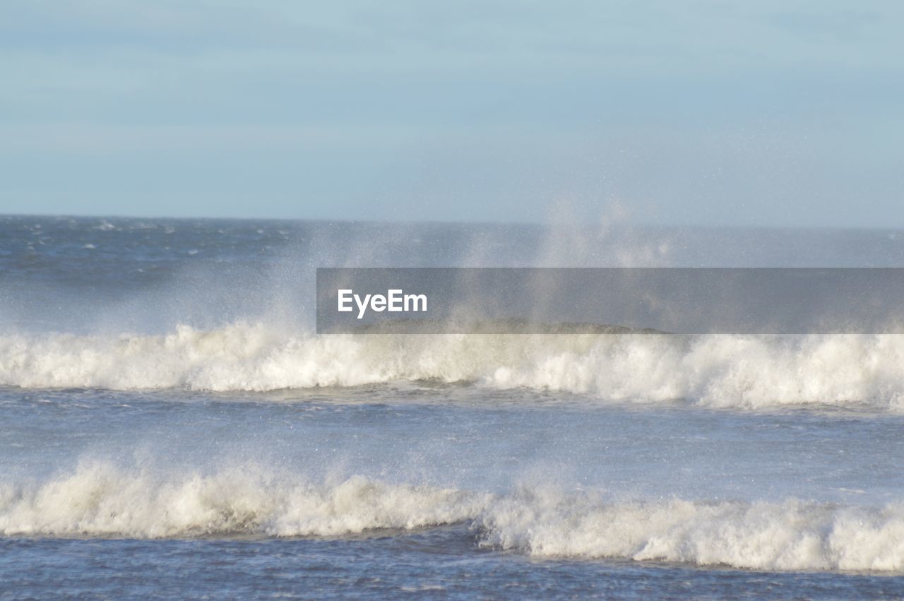 SEA WAVES SPLASHING ON SHORE AGAINST SKY