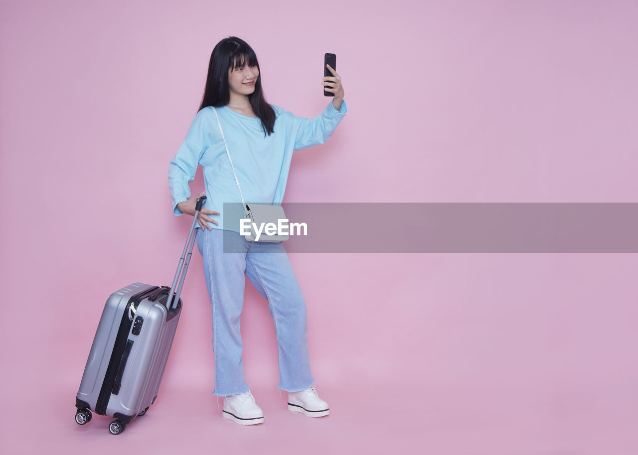 FULL LENGTH OF WOMAN USING MOBILE PHONE AGAINST PINK BACKGROUND