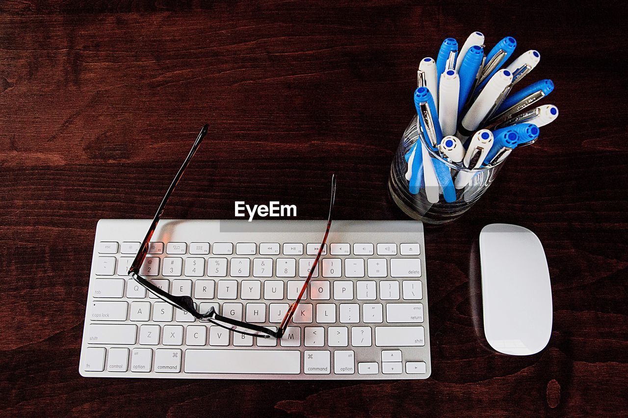 High angle view of keyboard with mouse and pens on wooden table