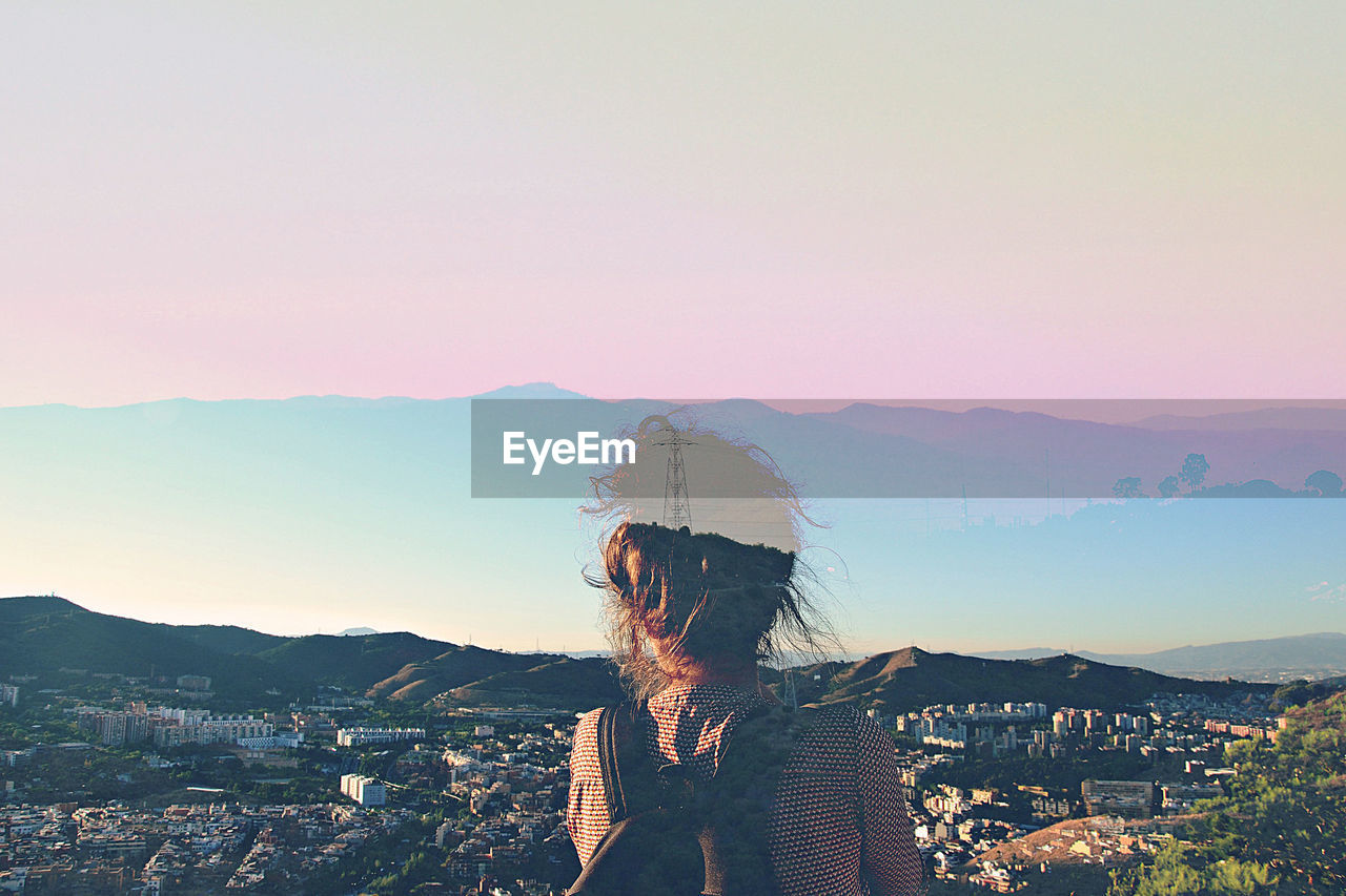 WOMAN STANDING BY BUILDINGS IN CITY AGAINST SKY