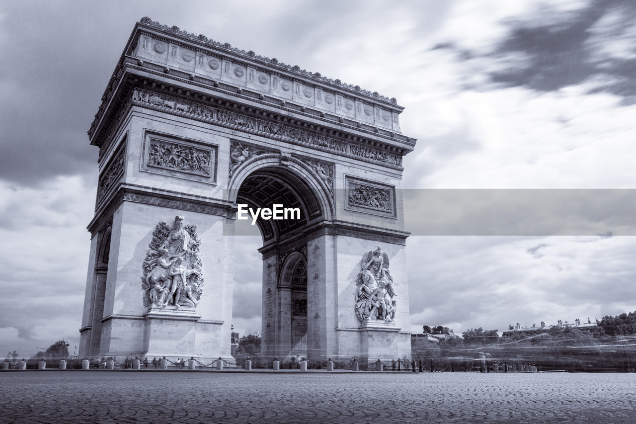 Low angle view of arc de triomphe against cloudy sky