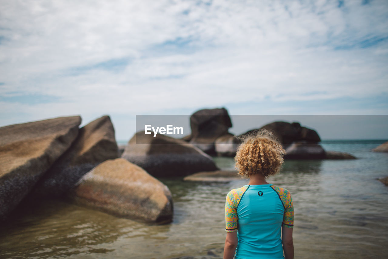 Rear view of woman standing at beach against sky