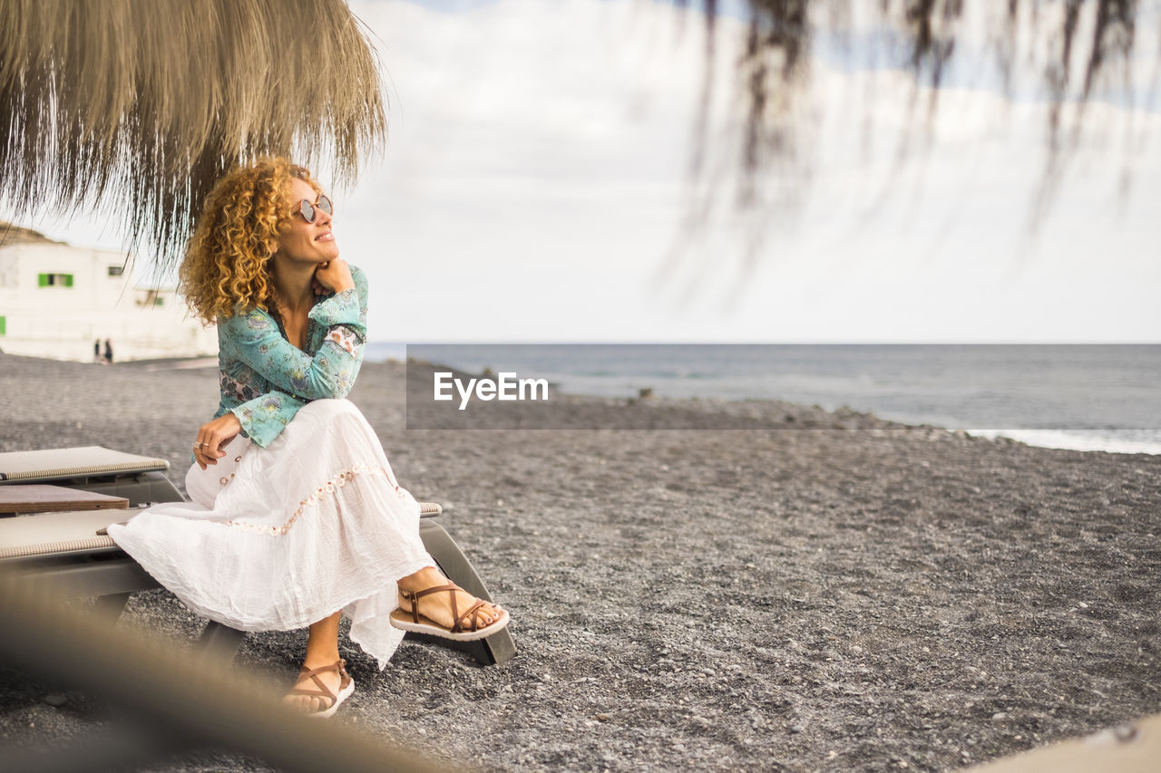 Smiling woman looking at sea while sitting on lounge chair