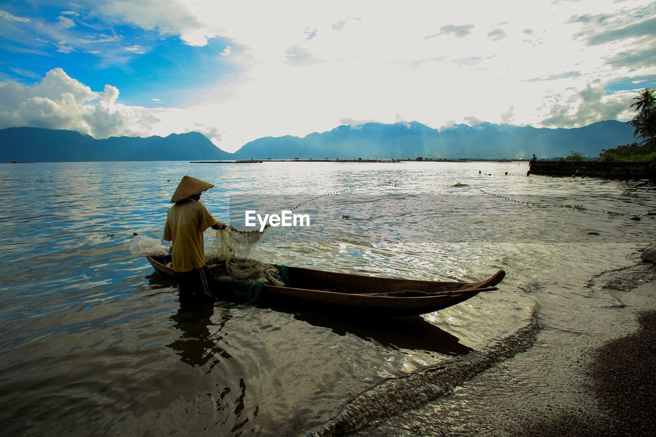 Man on boat in lake against sky