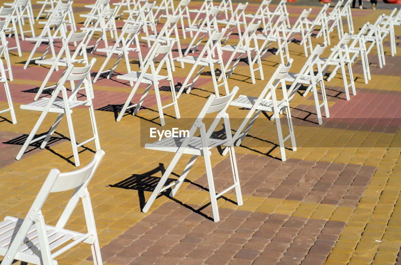 White folding chairs are placed on the square on pavement. quarantine restrictions