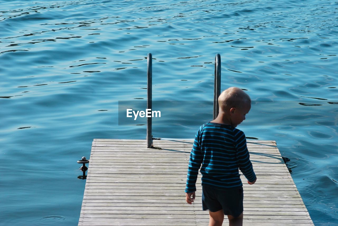 Rear view of boy standing on pier by lake