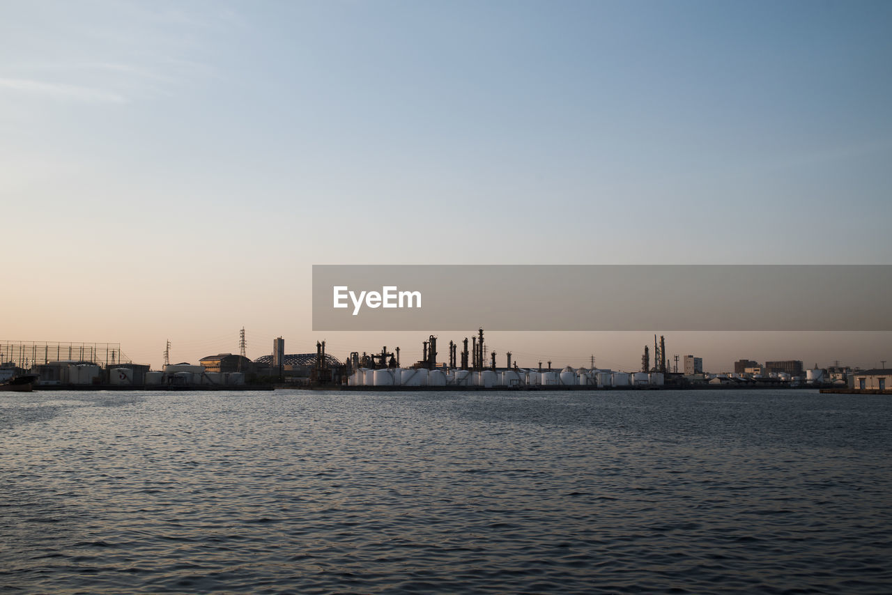 Silhouette buildings by sea against sky during sunset