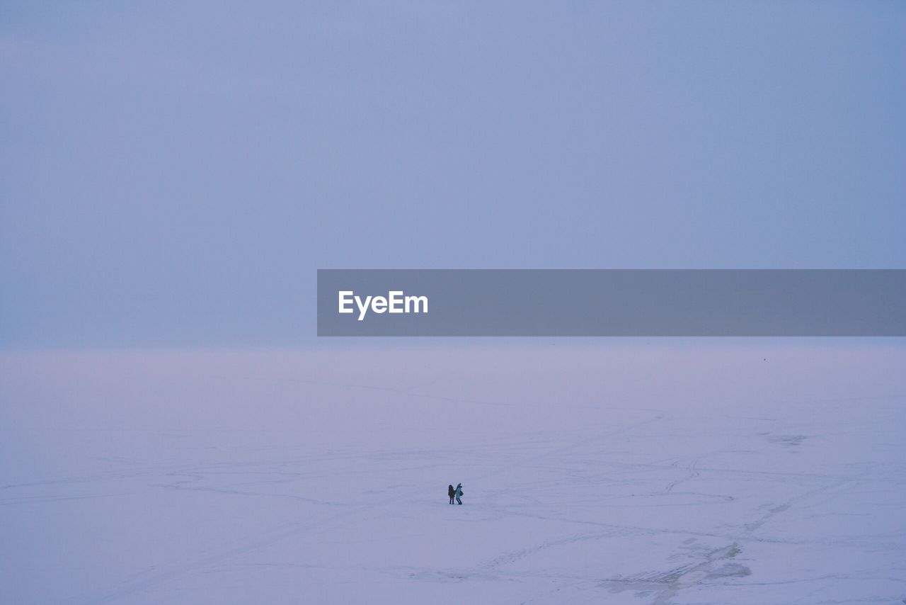 Distant view of people standing on snow covered field against clear sky