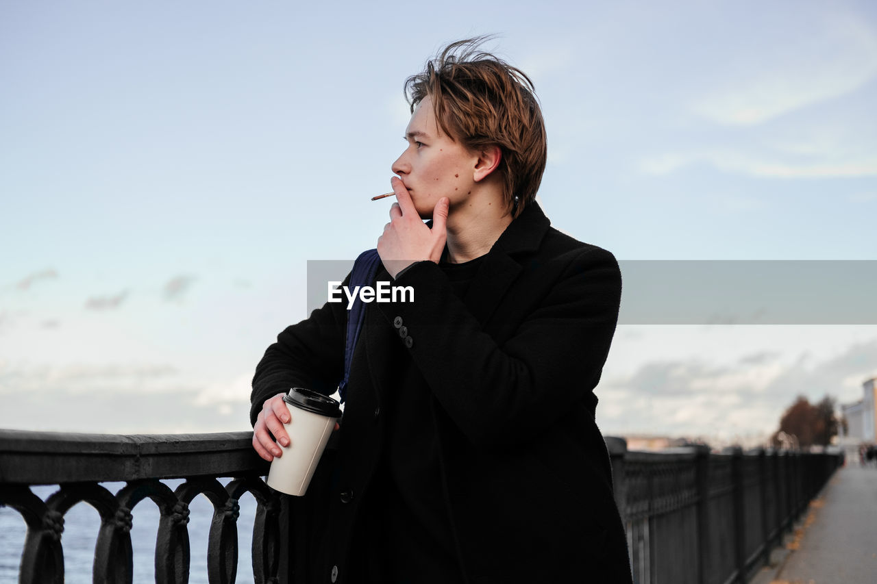 Young man smoking cigarette while standing outdoors