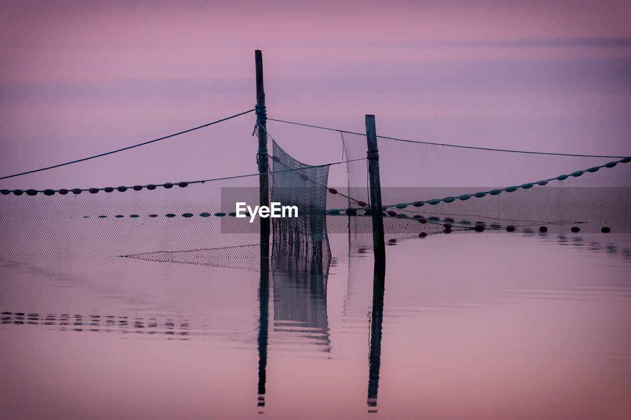 REFLECTION OF WOODEN POST IN SEA AGAINST SKY