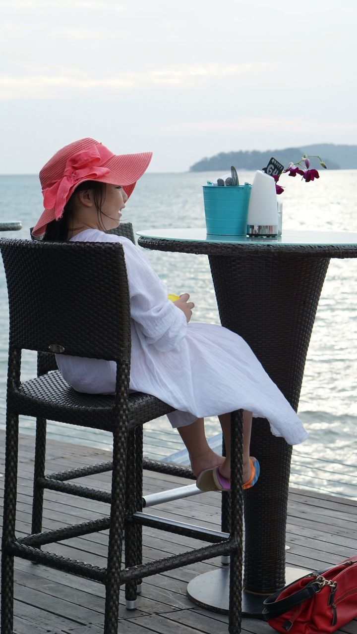 Woman sitting on chair at beach against sky