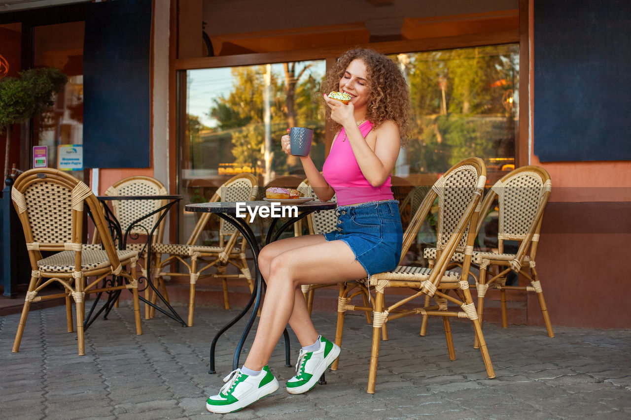 Young attractive curly woman sits at table in cafe on summer terrace. colorful 