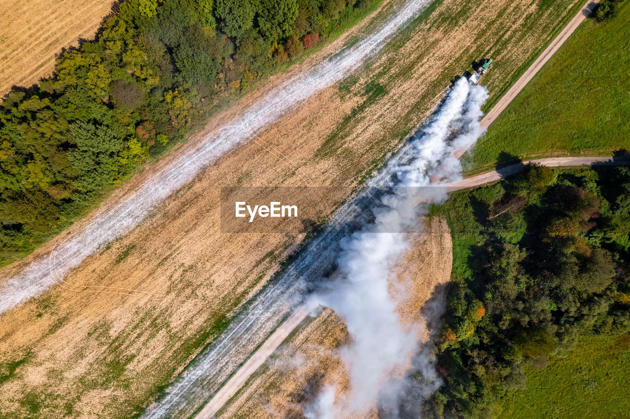 Aerial view of a tractor spreading lime on fields to improve soil quality after the harvest. 