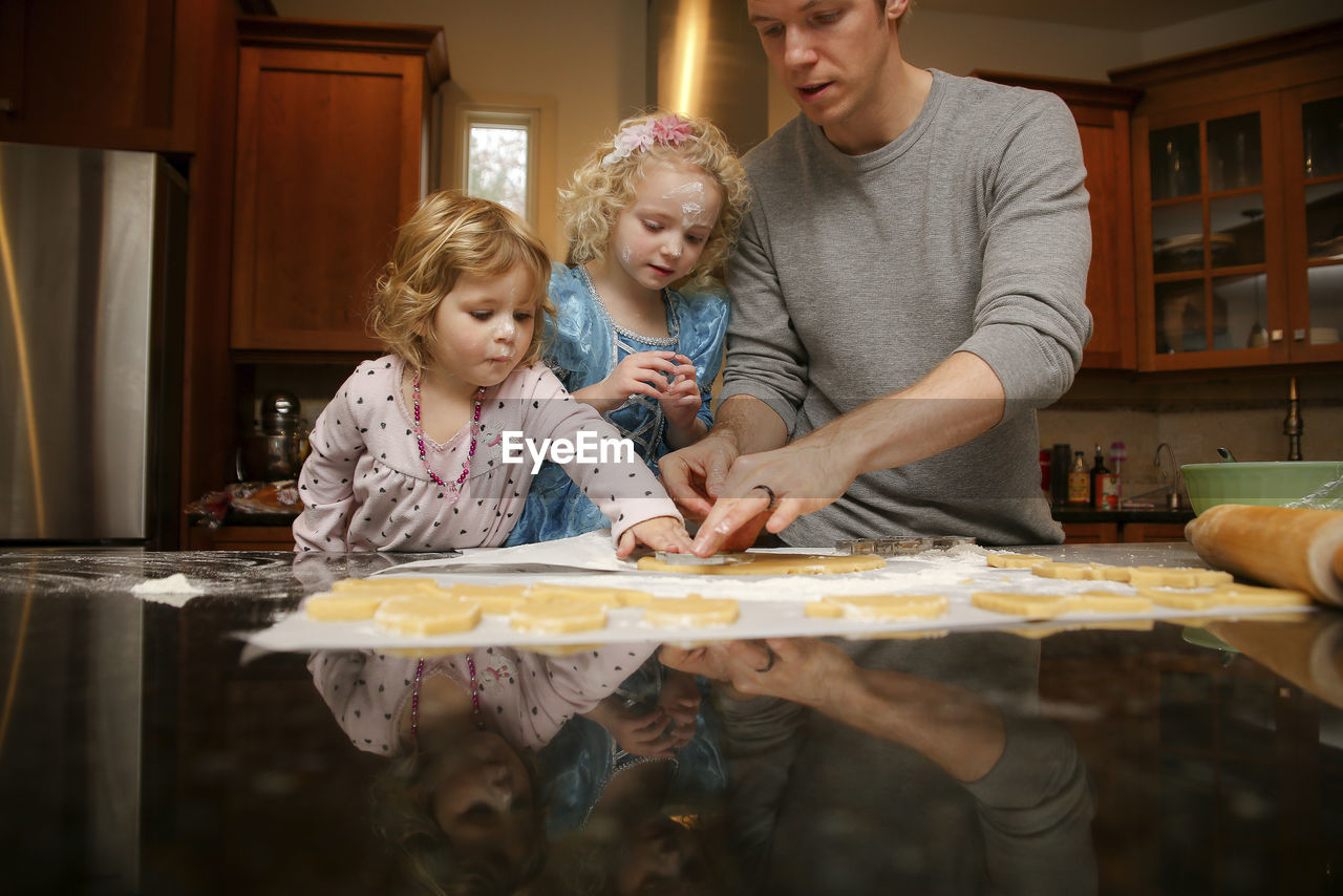 Father with daughters making cookies at table in kitchen