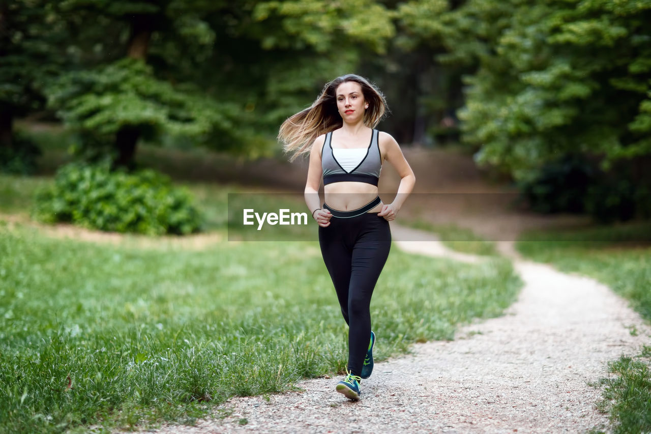 Beautiful young woman running on footpath amidst grassy field