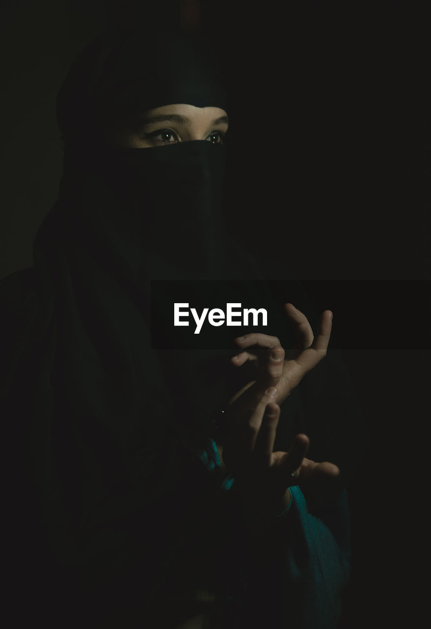 Young woman wearing hijab against black background