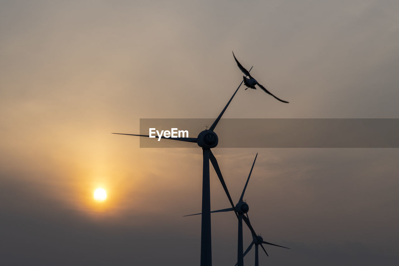 Low angle view of wind turbines against sky during sunset