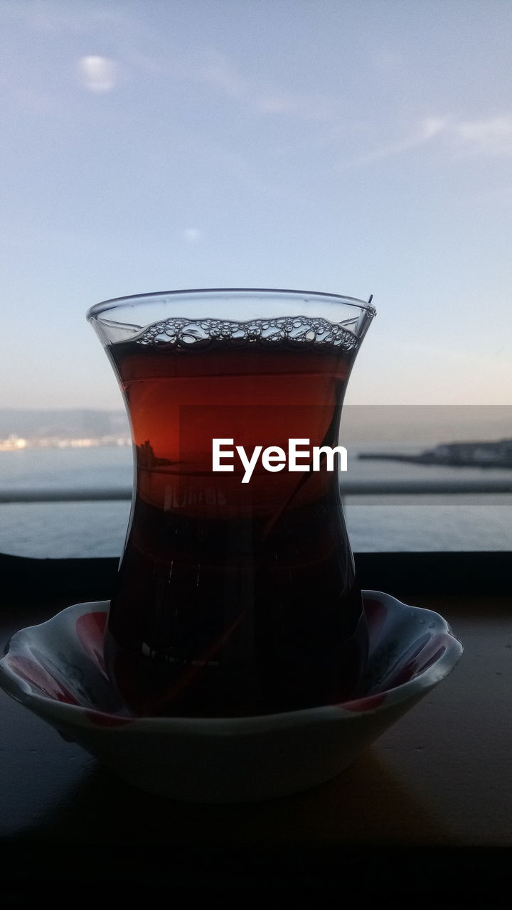 CLOSE-UP OF TEA IN GLASS ON TABLE BY SEA