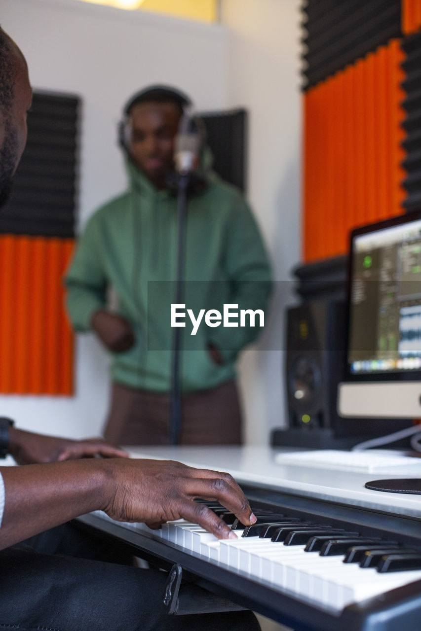 Hands of sound engineer playing piano while rapper standing in recording studio