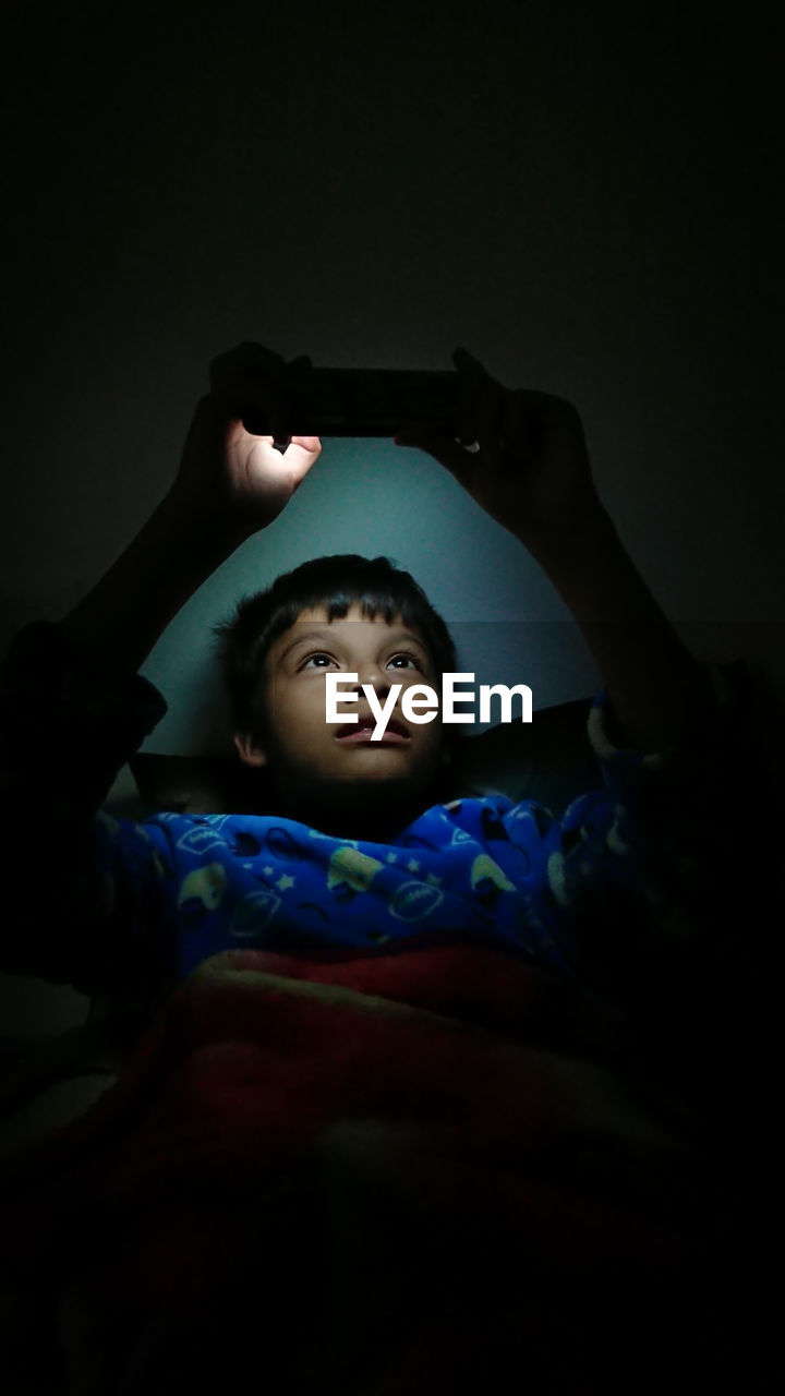 Boy using phone while lying in darkroom