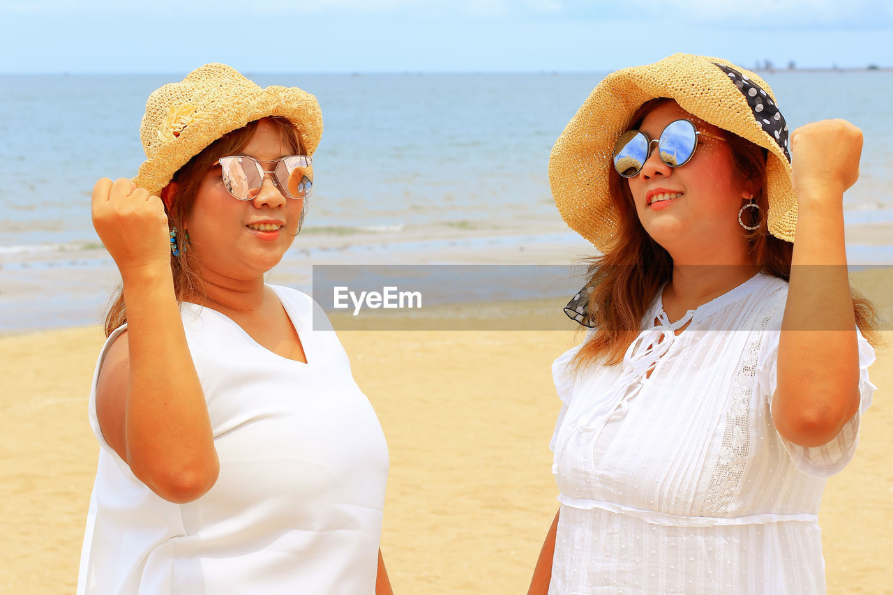 YOUNG WOMAN WEARING HAT WHILE STANDING AT BEACH