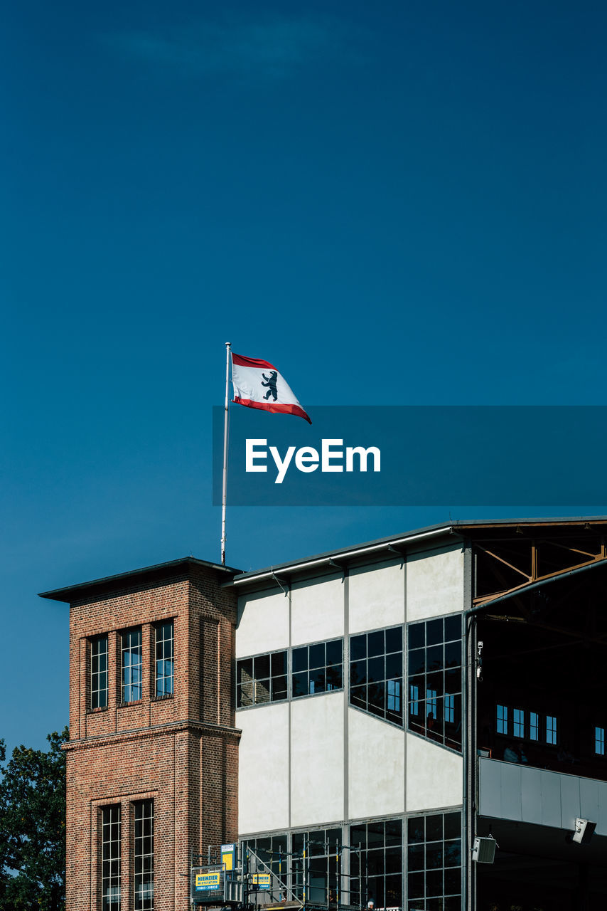 LOW ANGLE VIEW OF FLAG BY BUILDING AGAINST CLEAR BLUE SKY