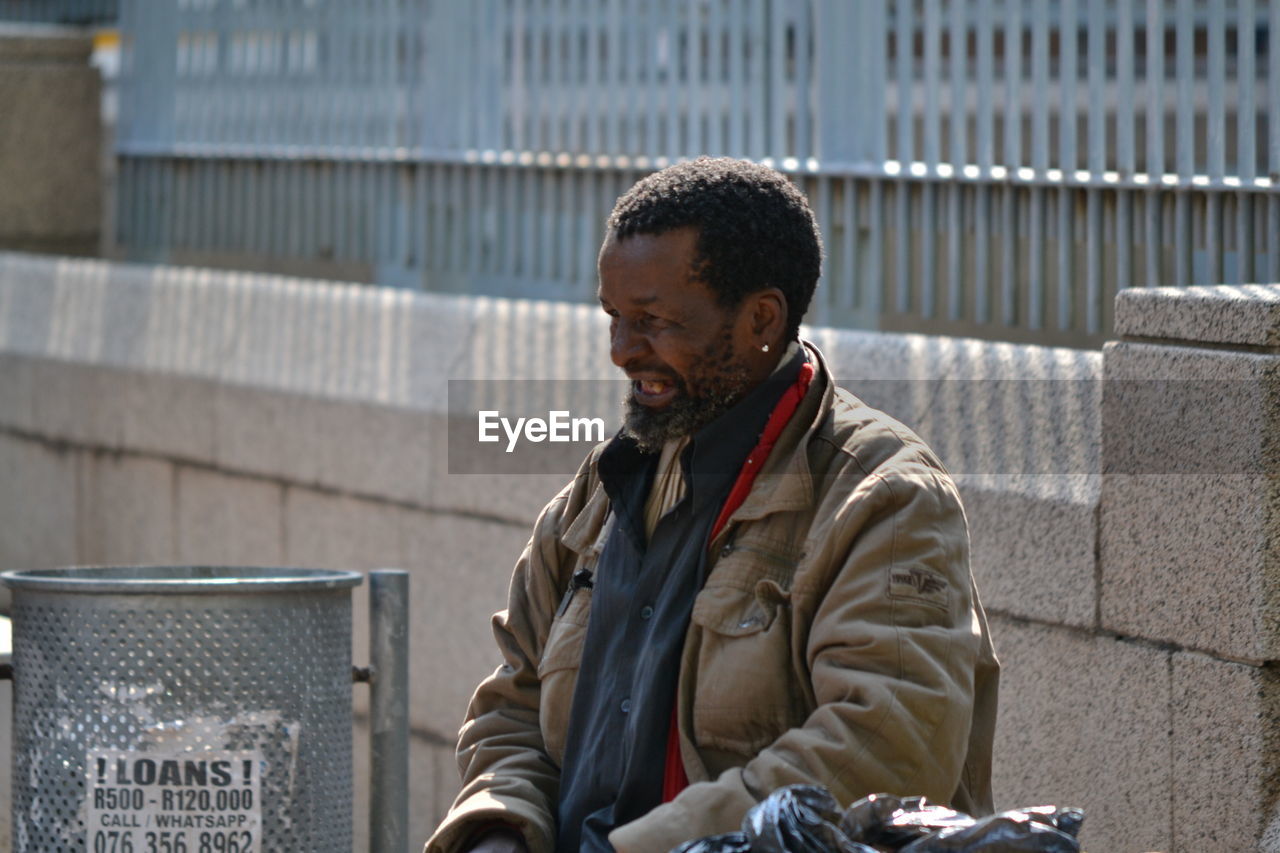 MAN LOOKING AWAY WHILE SITTING ON SIDEWALK