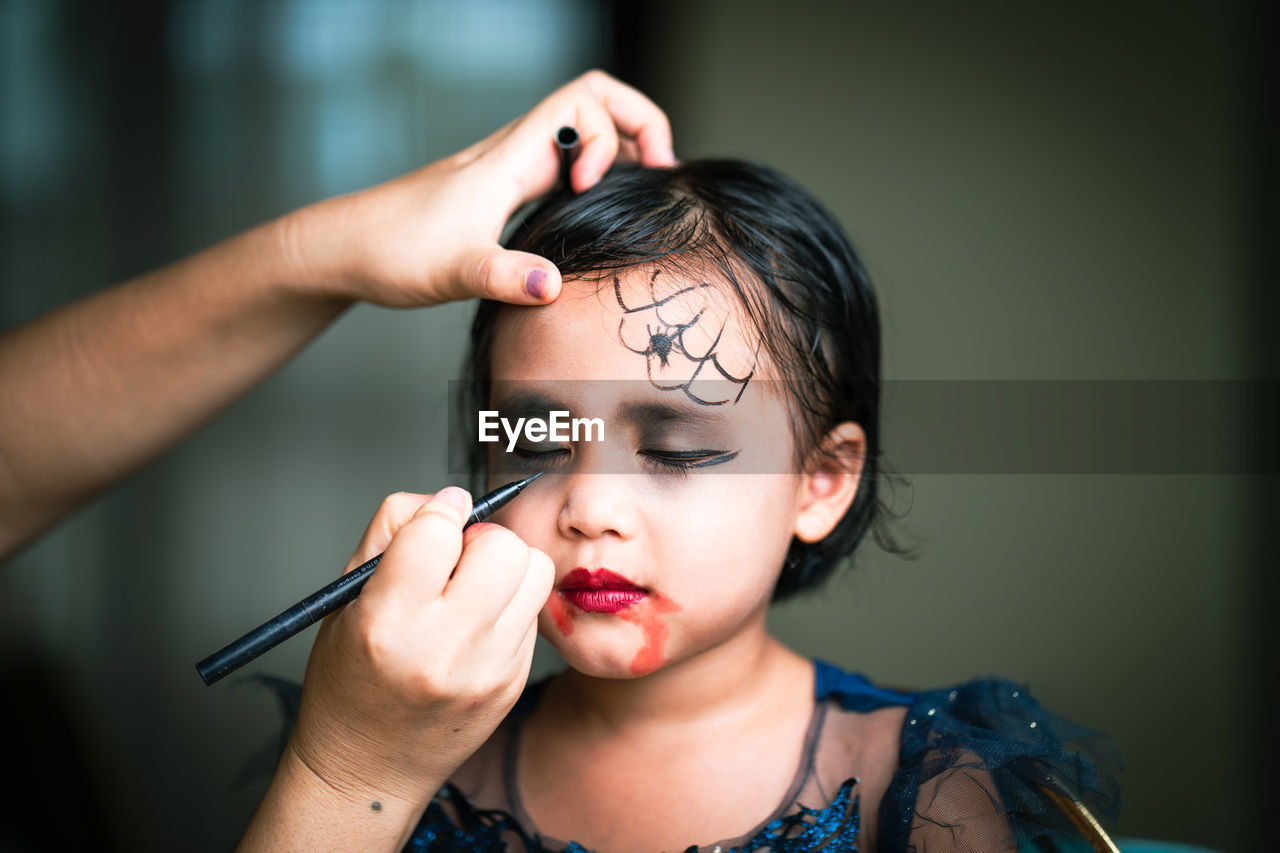 Mother painting daughters face. halloween party.
