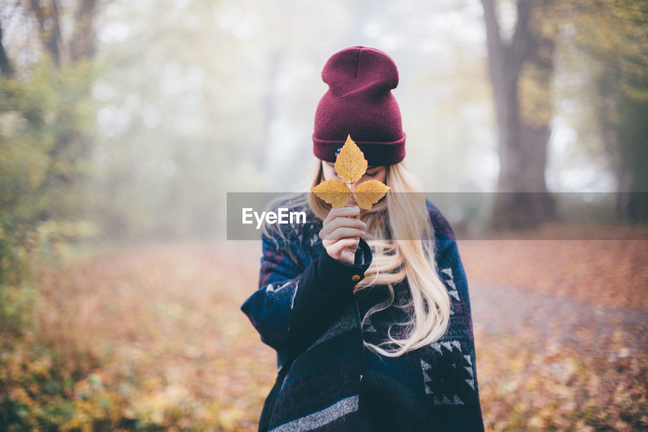 Woman holding leaf while standing on field during autumn