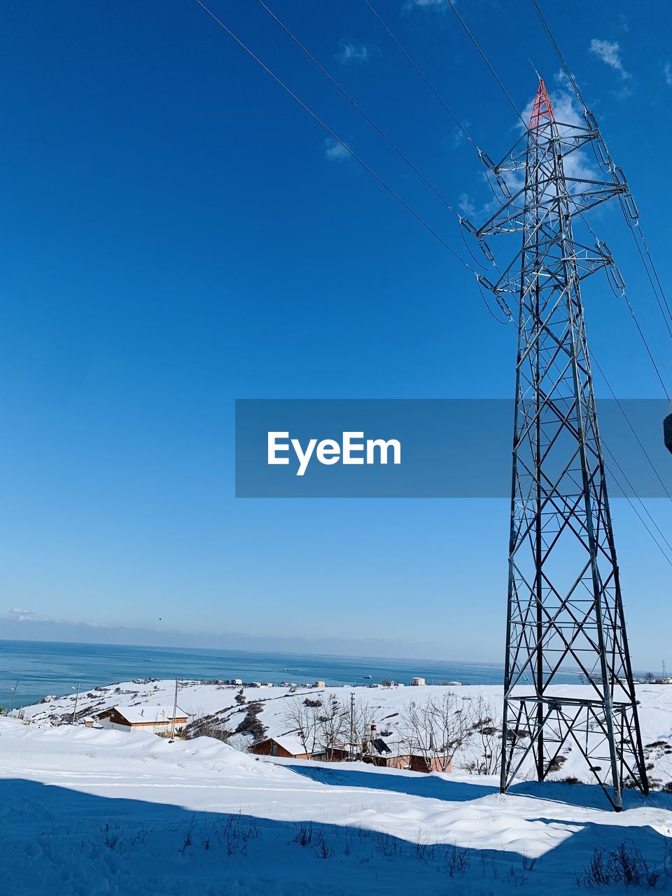 Electricity pylon on land against clear blue sky during winter