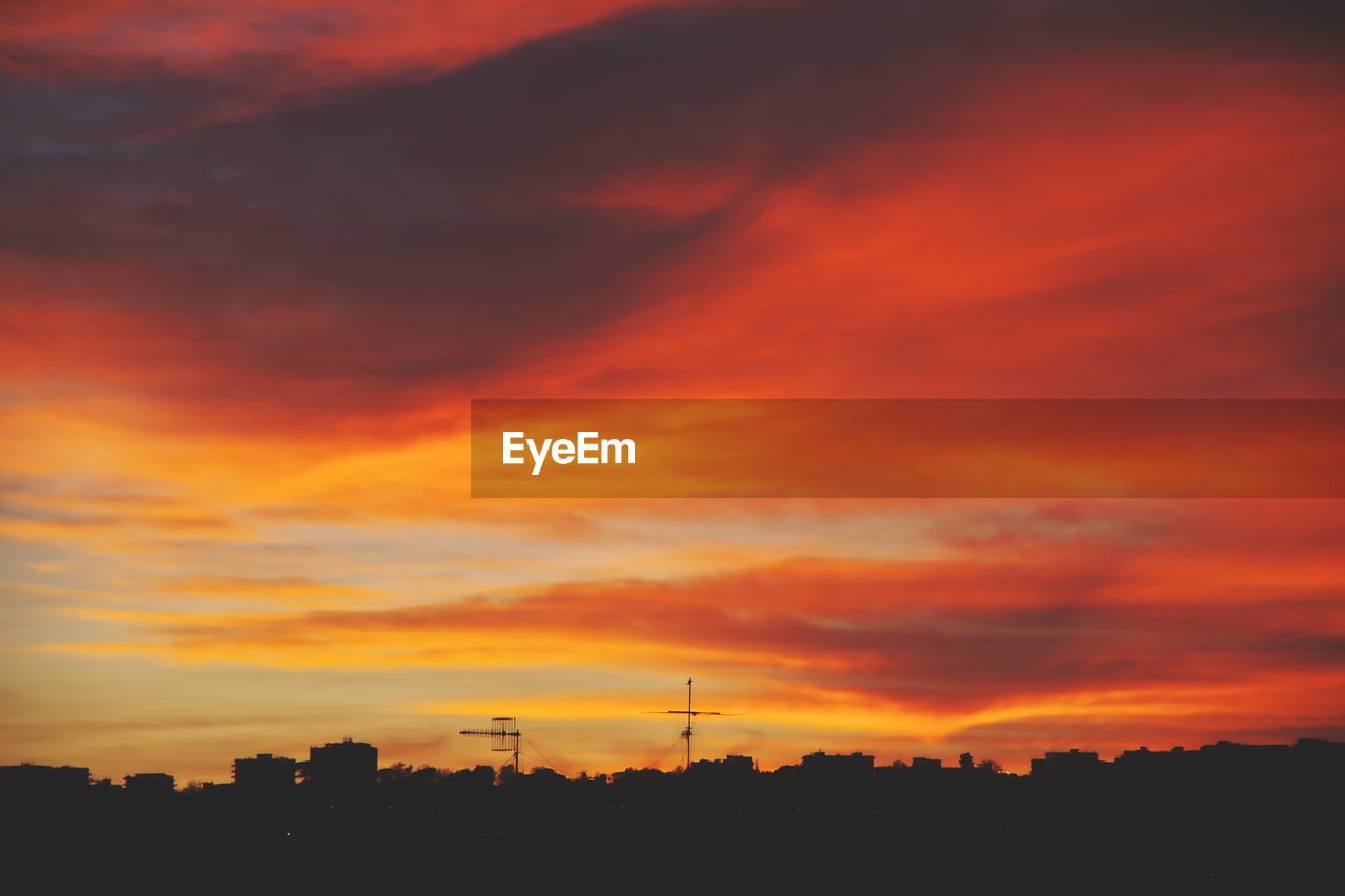 Silhouette of city against dramatic sky during sunset