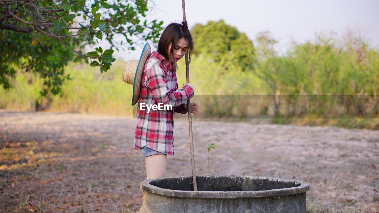 Young woman putting pole in well at farm