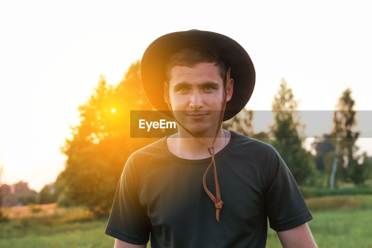 Young man farmer in cowboy hat at agricultural field on sunset with sun flare. closeup portrait 