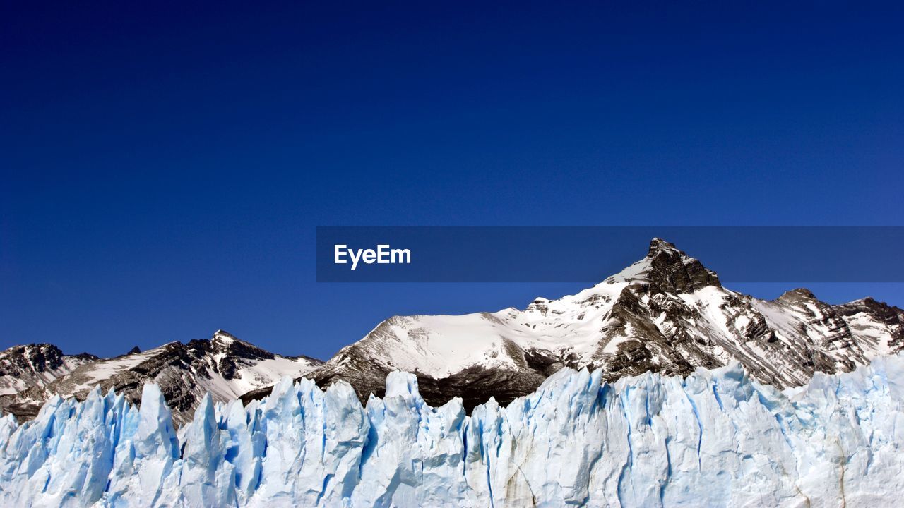 Panoramic view of snowcapped mountains against clear blue sky