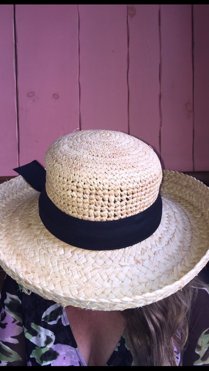 Close-up of woman with face covered by straw hat against wall