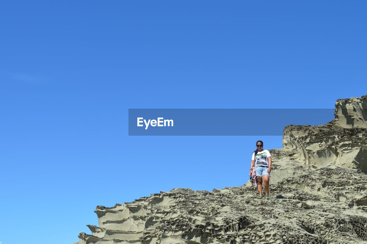 Low angle view of people standing on rock against clear blue sky