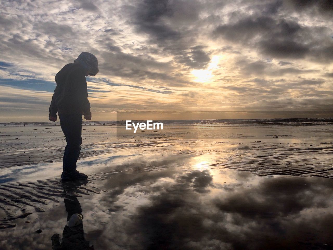 SILHOUETTE OF WOMAN STANDING ON BEACH AGAINST CLOUDY SKY