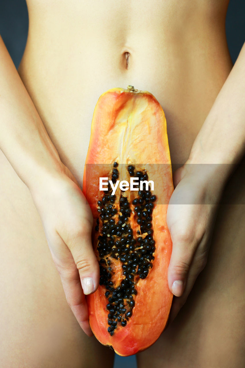 Midsection of naked woman holding halved papaya