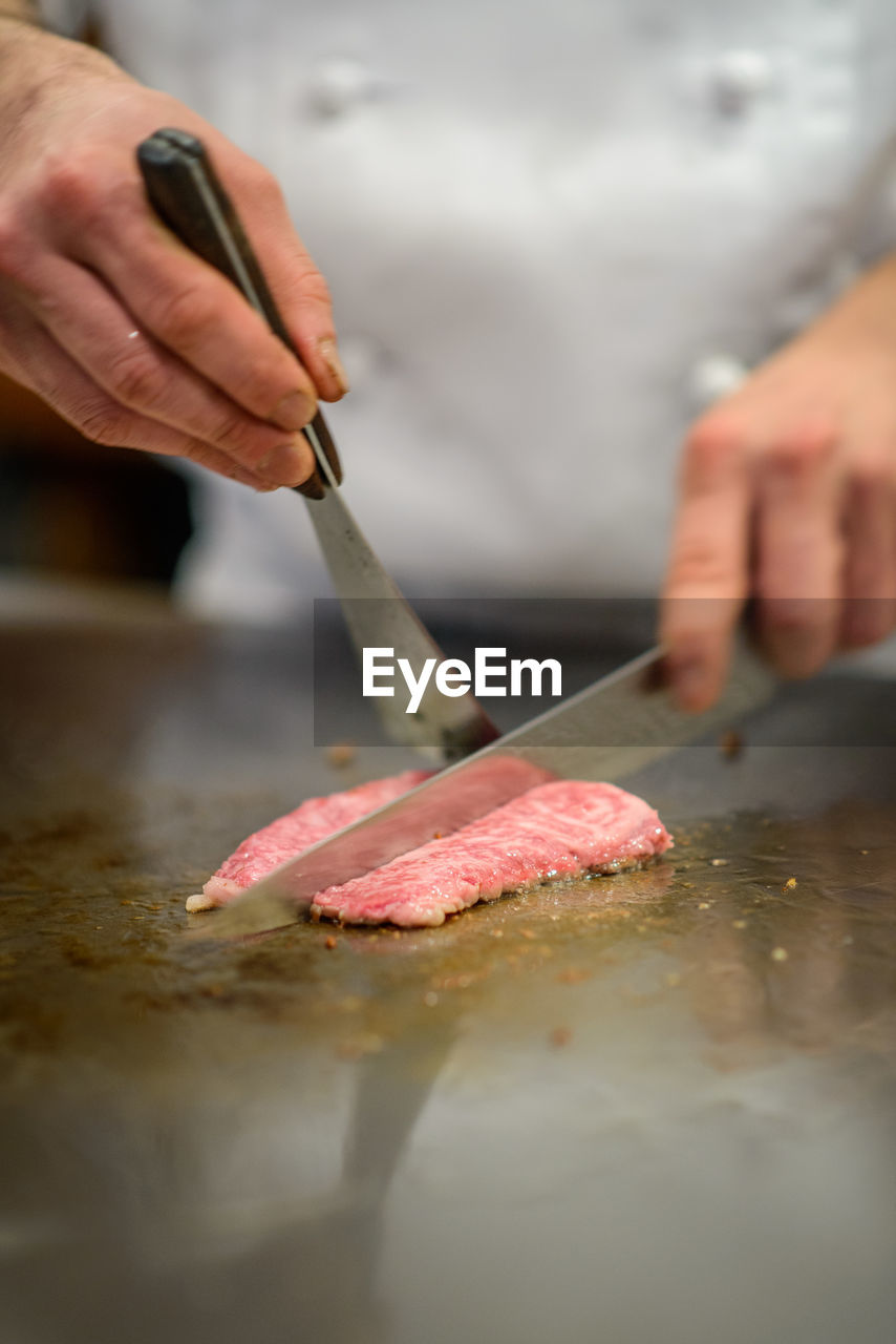 Close-up of chef's hand cutting and preparing steak