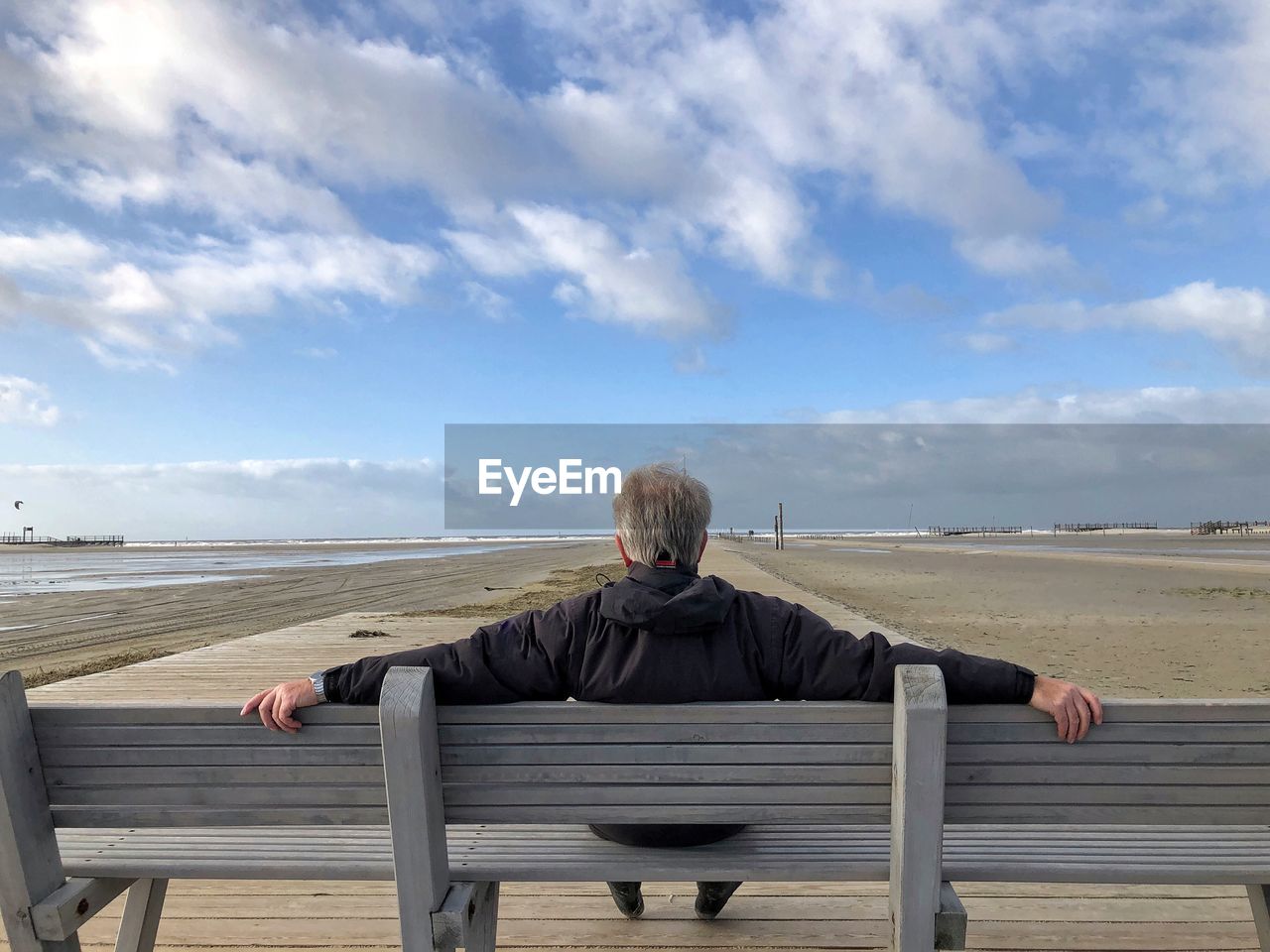 Rear view of man sitting on bench against sky