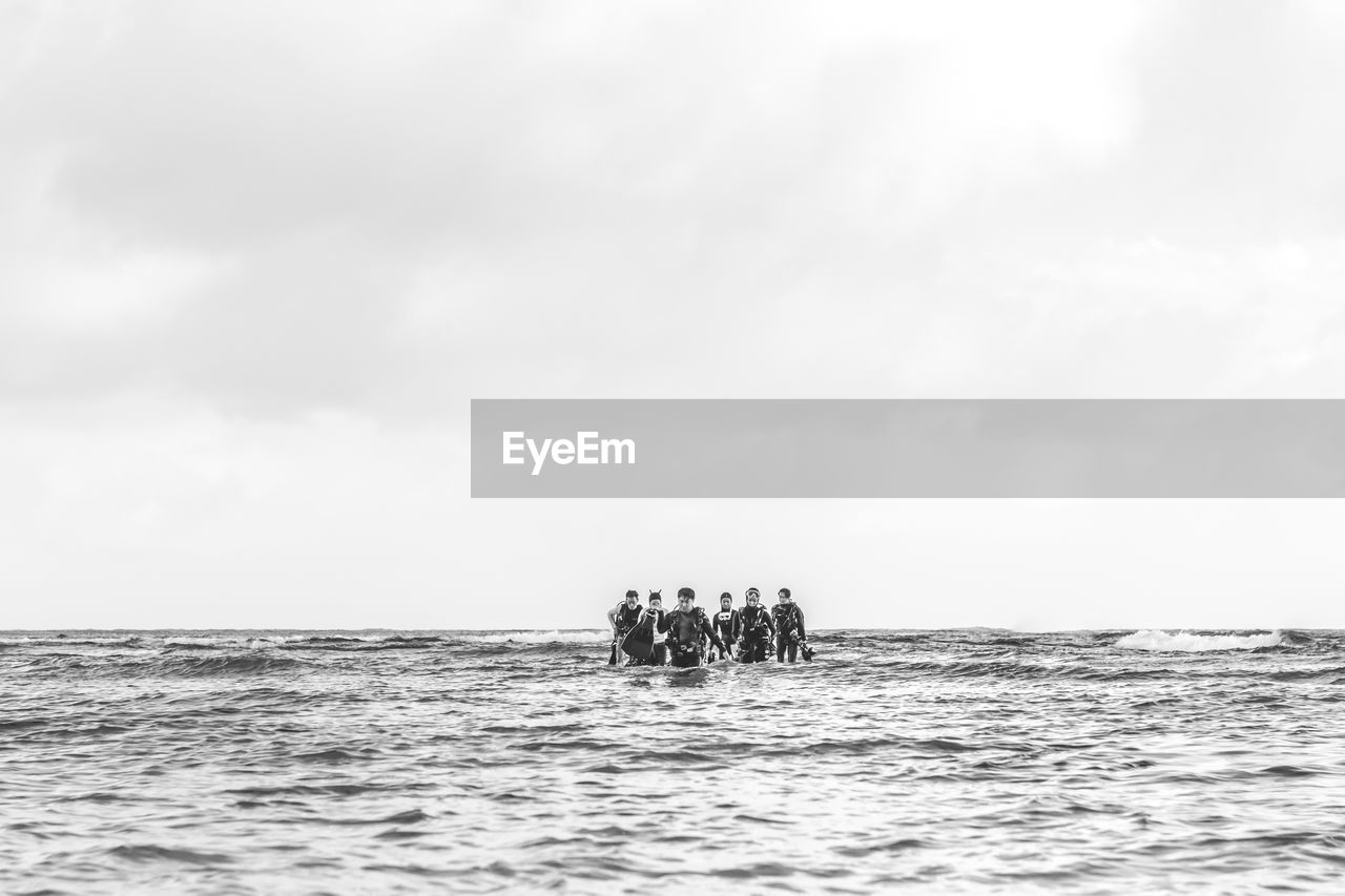 Mid distance view of scuba divers walking in sea against sky