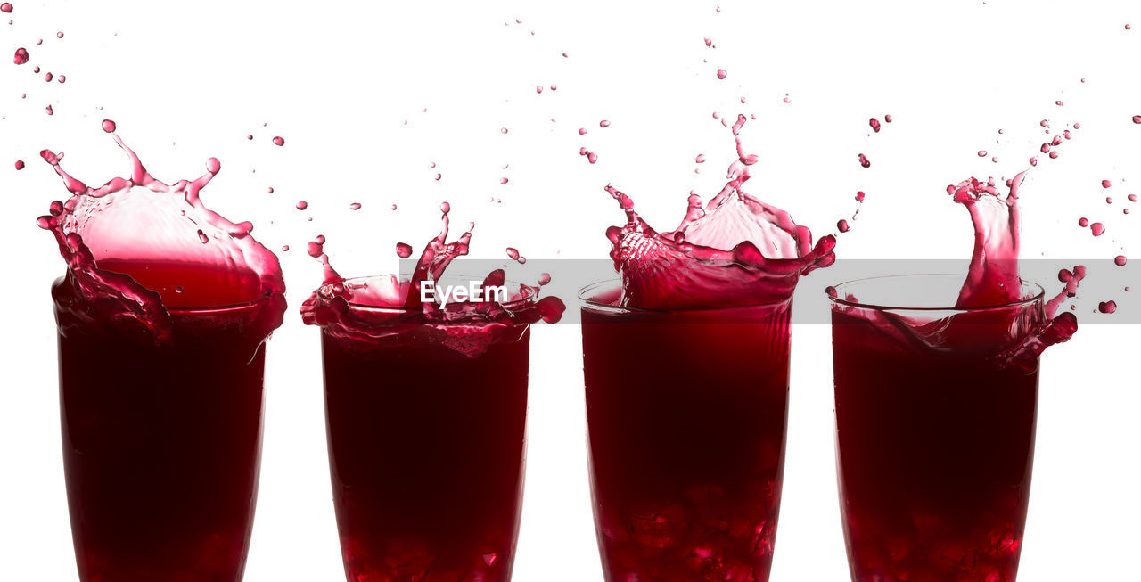 Close-up of splashing drink in glasses against white background
