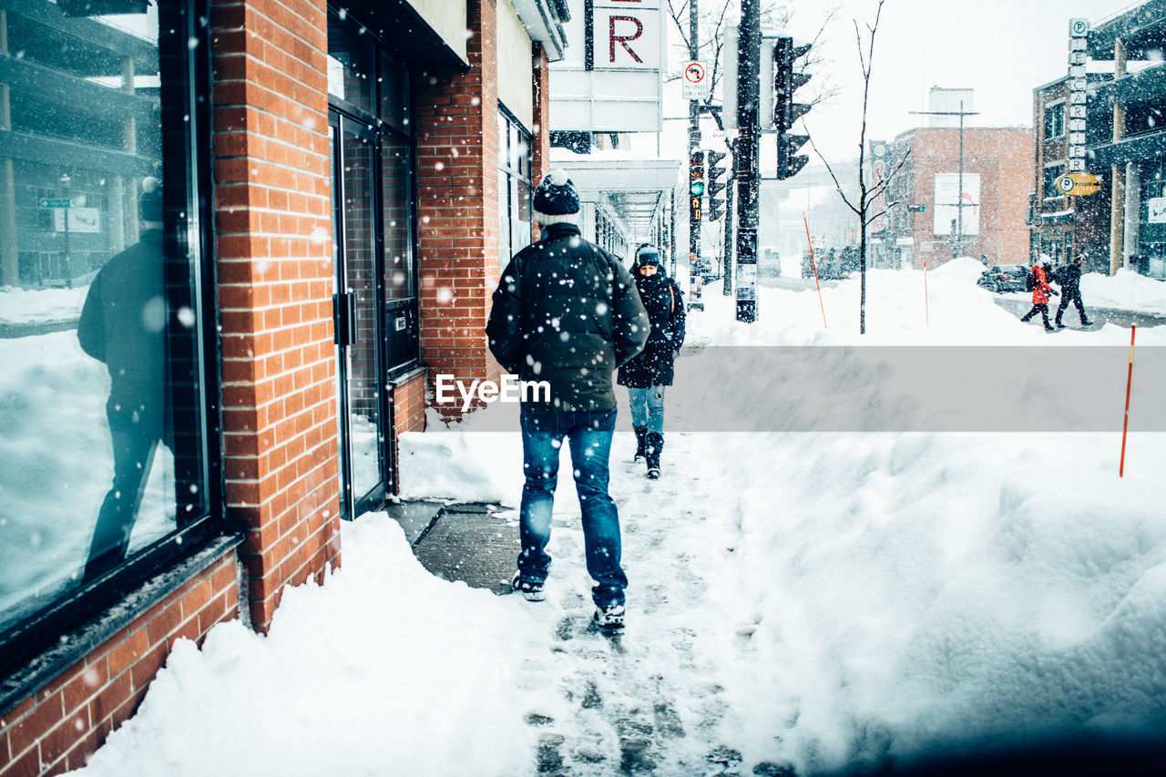 MEN WALKING ON SNOW COVERED CITY AGAINST SKY