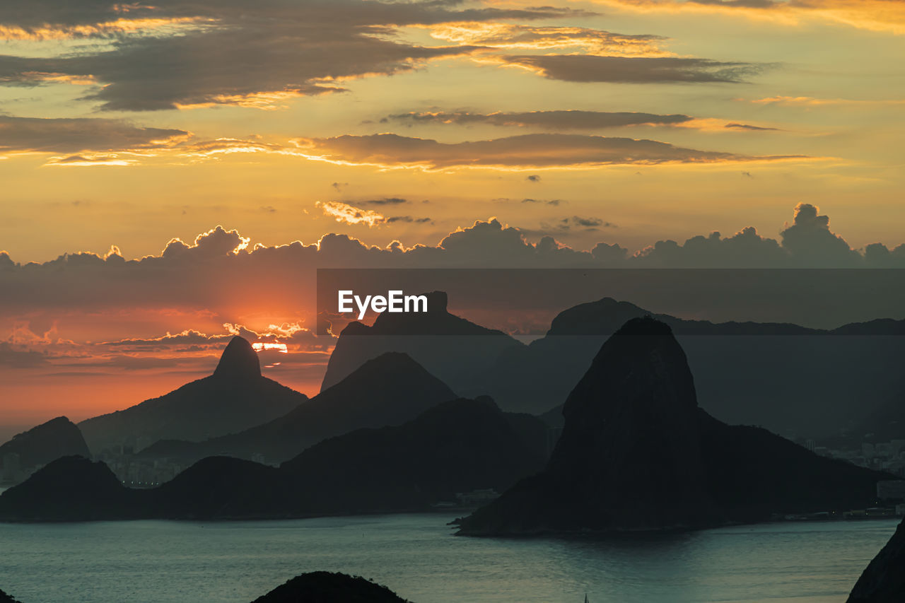 SILHOUETTE MOUNTAINS BY SEA AGAINST SKY DURING SUNSET